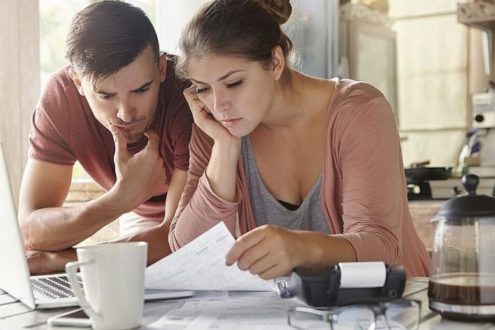 Young female and her unemployed husband with many debts doing paperwork together in kitchen, reading notification, informing that they must move out from their apartment because of non-payment