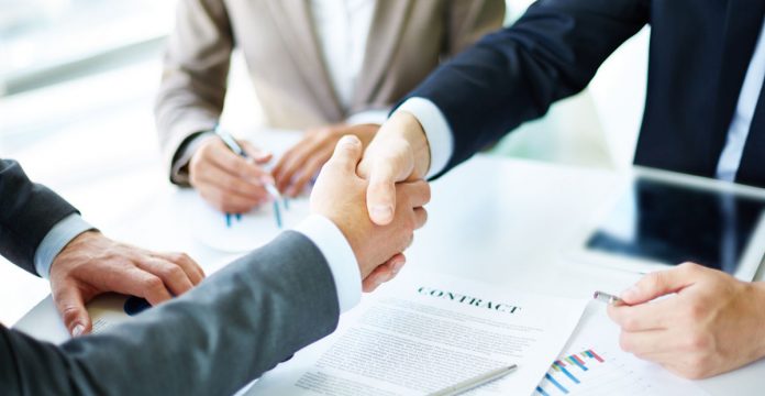 Image of business partners handshaking over business objects on workplace
