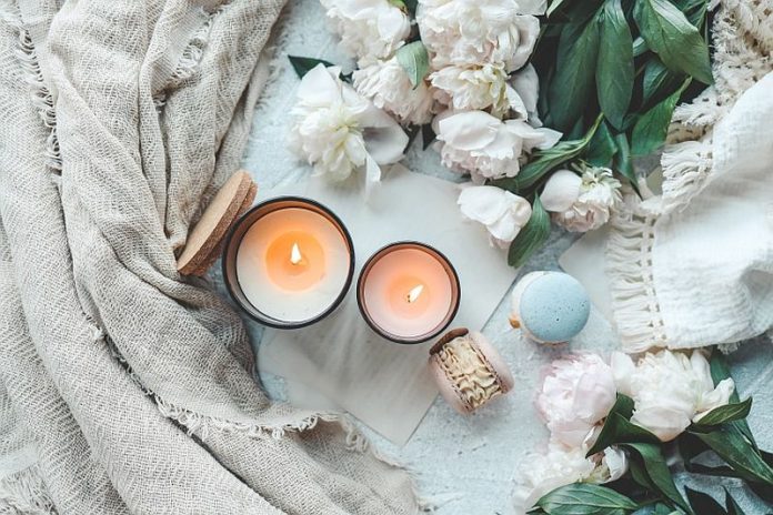 Two burning candles in a cozy home interior, white peonies and macarons